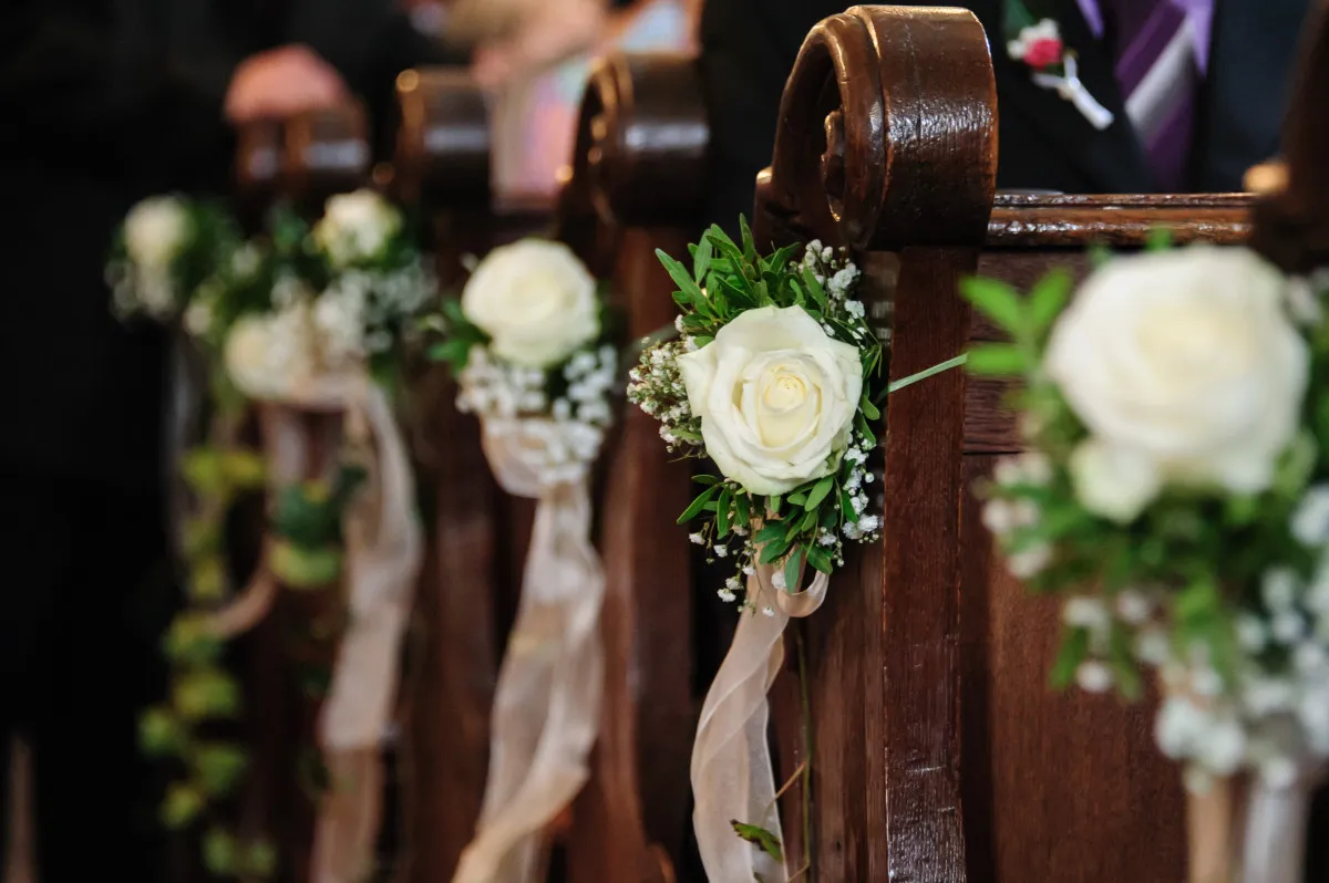 Arreglos florales de rosas blancas y paniculata en los bancos de la iglesia para una boda