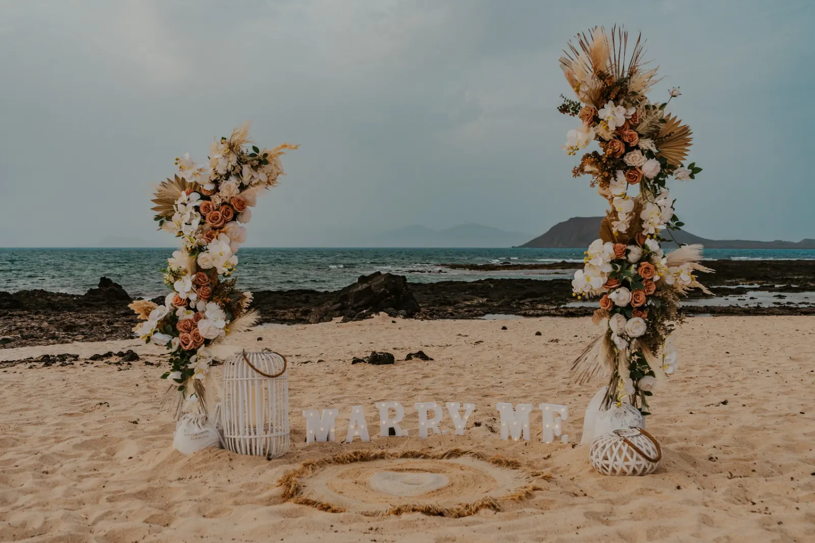 Arco floral en la playa con letrero luminoso Marry Me