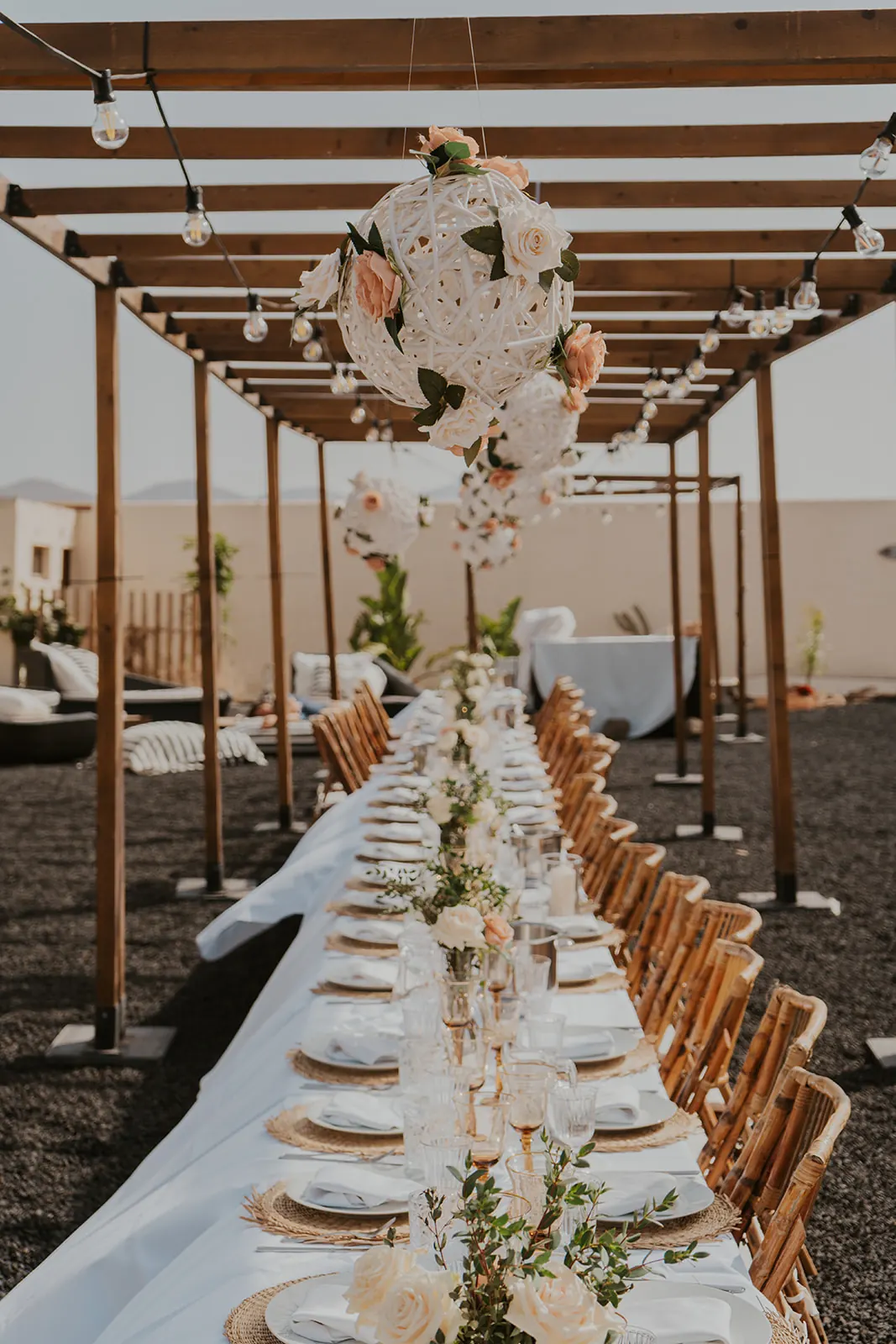 Pérgola de madera con mesa larga decorada con esferas de flores blancas y rosas